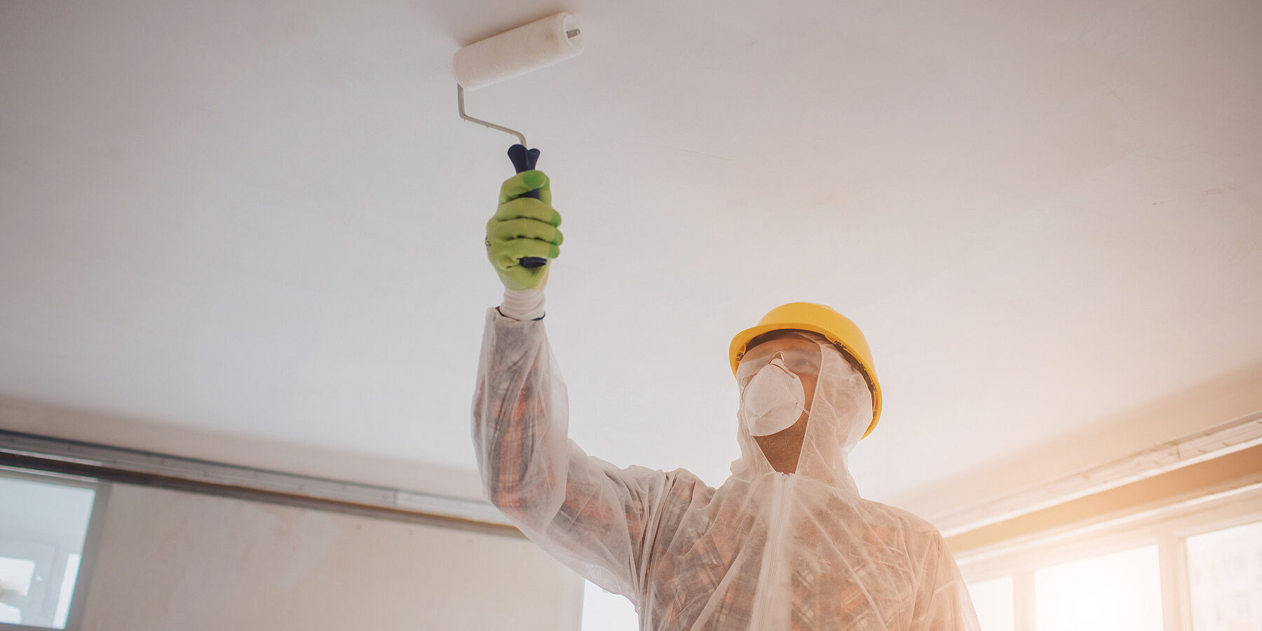 The builder works at the construction site . Worker with a paint roller. He is wearing a protective suit and mask for a face