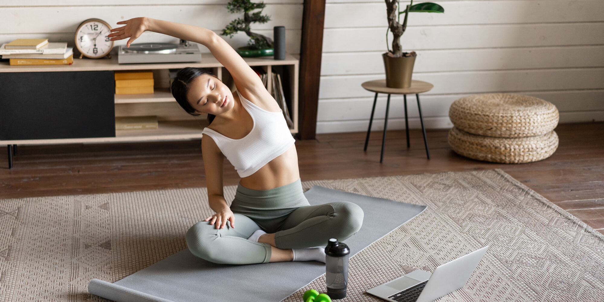 Young asian fitness girl doing stretching, sport workout at home, stretch arms and looking at laptop, follow exercise video on computer